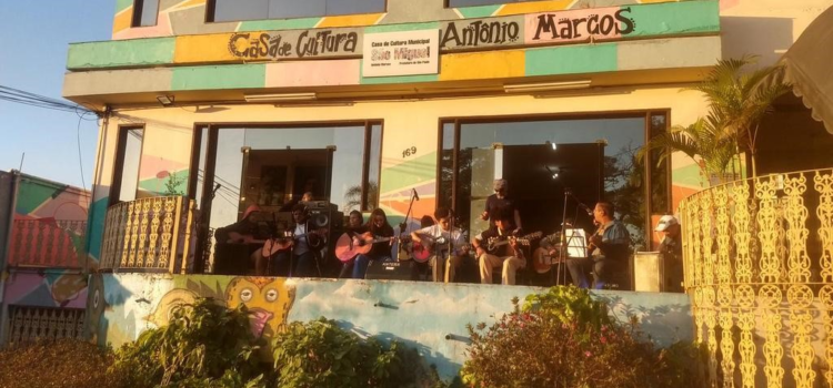 Imagem da sacada da Casa de Cultura São Miguel. Na sacada, há jovens em uma oficina de violão.